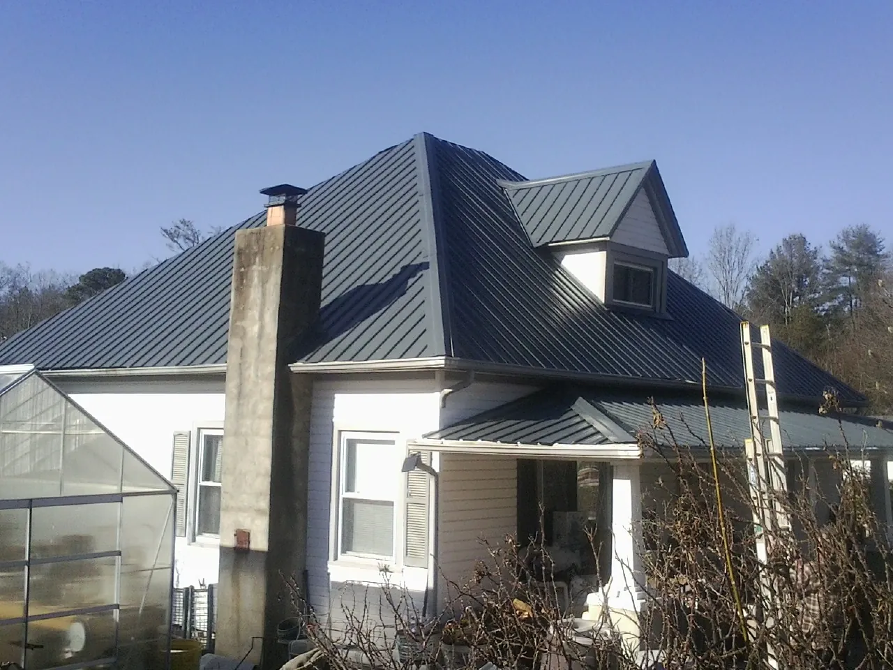 Dark blue standing seam metal roof on a white farmhouse with dormer — Slate & Tile Roof Repair by Roofing Brothers in Wind Ridge