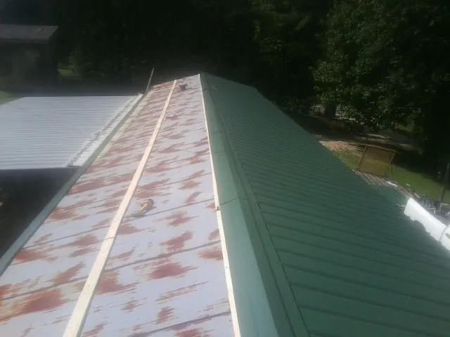 Old rusted panels beside newly installed green metal roofing — Wind Damage Roof Repair by Roofing Brothers in Wind Ridge