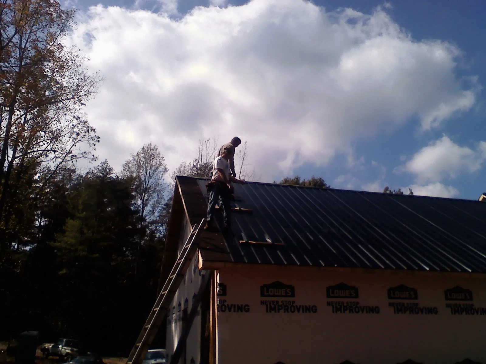 Roofer fastening dark metal panels high against a cloudy sky, from a Roof Inspection job in Wind Ridge