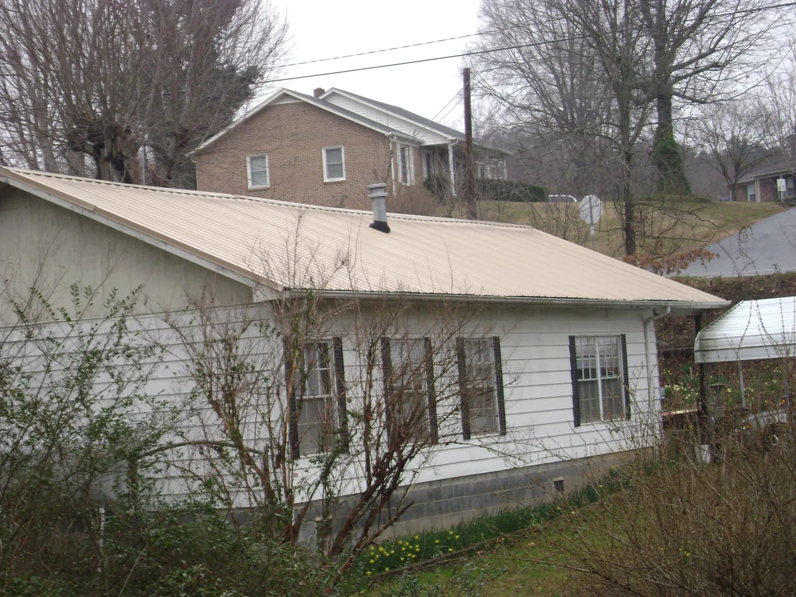 Tan metal roof on a white sided house set into a hillside — Commercial Roofing by Roofing Brothers in Wind Ridge