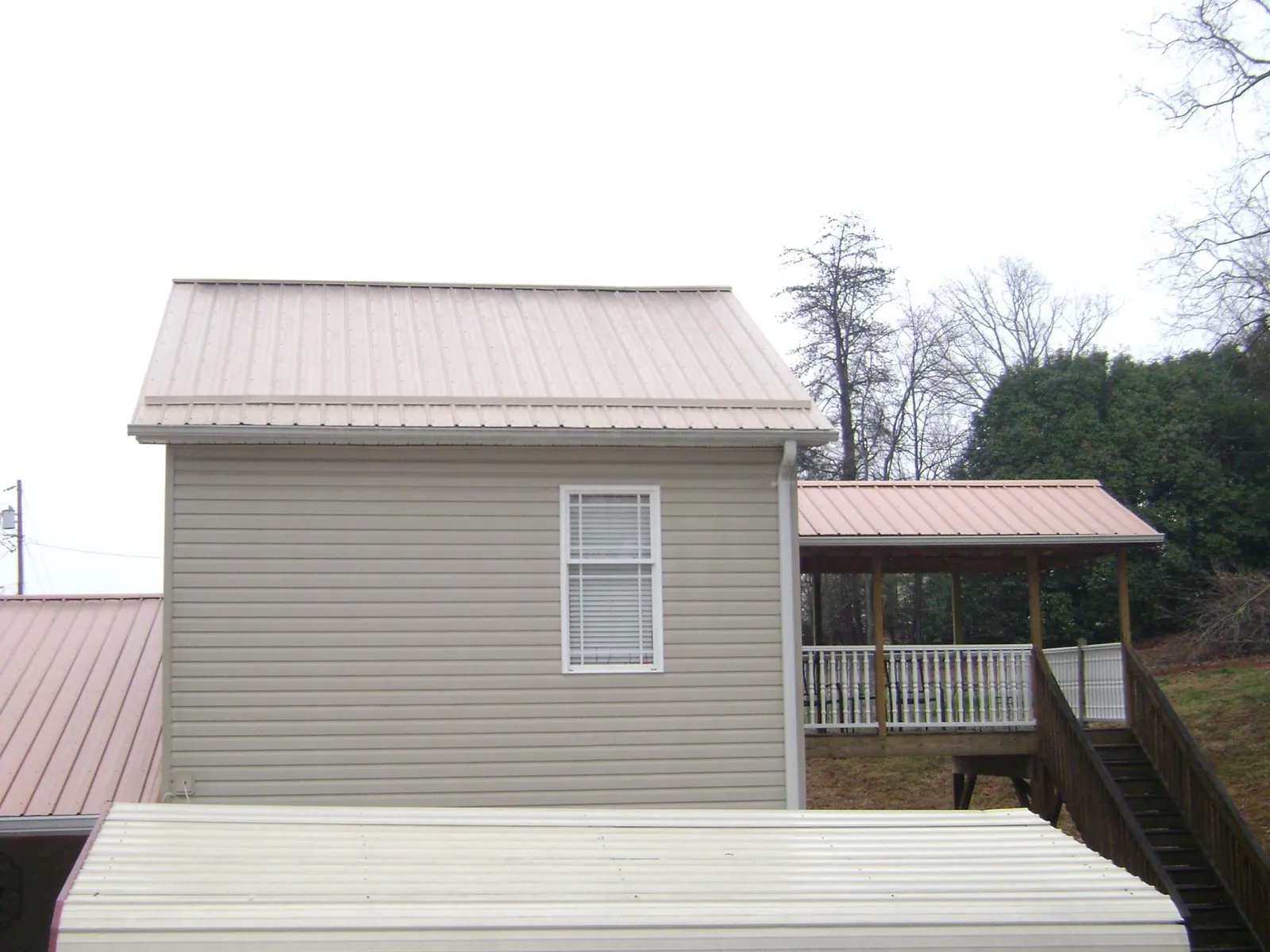 Tan metal roofs on a two story addition and attached porch, from a Roof Replacement job in Wind Ridge